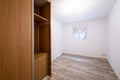 Renovated room with built-in wardrobe with sliding doors in cherry wood color, interior chest of drawers, white aluminum window Royalty Free Stock Photo