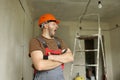 Renovation apartment. Young tired foreman constructor repairman with crossed hands in protective helmet and overalls is