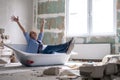 Renovation home. Excited woman sits in bathtub in the middle of the room raising arms. Empty walls, repairs house with Royalty Free Stock Photo