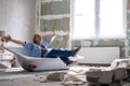 Renovation home. Excited woman sits in bathtub in the middle of the room raising arms. Empty walls, repairs house with Royalty Free Stock Photo