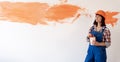 Renovation of a new house woman repairman with a brush painted the wall with paint. Caucasian girl in an orange hard hat