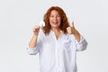 Rent, buying property and real estate concept. Cheerful and pleased middle-aged redhead woman showing house card and