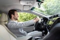 Stylish guy in suit driving in city with hand on steering wheel, empty space