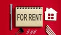 FOR RENT text written on a notebook with pencils and office tools and model wooden house Royalty Free Stock Photo