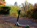 Rentable green electric city scooter left along the side of asphalt sidewalk