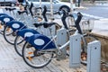 Rental E-bikes, bicycles assisted by electric motors, are parked in a row at a docking port in the city street. Modern