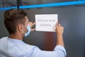 Reopening business. Rear view of a young man in protective face mask sticking open sign with text OPEN AS NEW NORMAL on