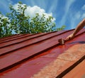 Repainting old metal roof with a paint brush and red paint. Roofer painting house metal roof with red paint