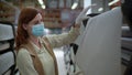 Repair coronavirus, young woman in mask and gloves chooses wallpaper in hardware store during isolation and pandemic