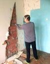 Repair in the home. A young man knocks down old Soviet-era plasterboard slabs from the wall with iron scrap. Visible brick wall ba