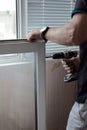 Repair of PVC windows. A worker installs a new pvc window mechanism using a drill. Selective focus, shallow depth of field