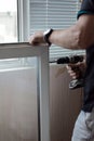 Repair of PVC windows. A worker installs a new pvc window mechanism using a drill. Selective focus, shallow depth of field Royalty Free Stock Photo