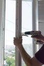 Repair of PVC windows. A worker installs a new pvc window mechanism using a drill. Selective focus, shallow depth of field Royalty Free Stock Photo