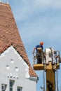 Repair and reconstruction of the old roof made of red tiles of a century-old building. The worker is in the basket of a crane and