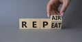 Repair and Repeat symbol. Hand turns cubes and changes the word Repeat to Repair. Beautiful grey background. Businessman hand.