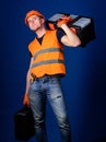 Repair service concept. Man in helmet, hard hat holds toolbox and suitcase with tools, blue background. Worker, repairer