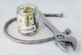 Repair word, coins and dollar bill in glass jar near flexible metal braided hose for plumbing taps and metal adjustable wrench on