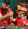 Repair and workshop concept. Father, parent with beard teaching little son to use tool screwdriver. Boy, child busy in