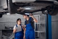 Two workers inspect a car raised on lifts