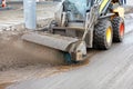 A compact road grader cleans a section of the road from dirty slurry with a nylon brush