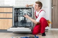 Repairman checks operating state of dishwasher in kitchen