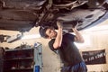 Repair man fixing car in repair station under lifted car during repair in garage