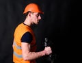 Repairman holds dumbbell in his right hand, black background. Strong builder concept. Builder in helmet working out