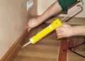 Repairman Installing Skirting Board Oak Wooden Floor with Caulking Gun Glue from Cartridge. Royalty Free Stock Photo