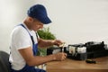 Repairman with magnifying glass and screwdriver fixing modern printer indoors