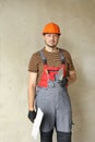 repairman in overalls and protective orange helmet holds two spatulas for plastering concrete wall with putty using Royalty Free Stock Photo