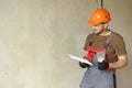 repairman in overalls and protective orange helmet holds two spatulas for plastering concrete wall with putty using Royalty Free Stock Photo