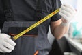 Repairman in uniform gloves measures tape measure