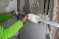 The repairman uses an aluminum ruler to level plaster on a concrete wall. In the foreground there is a bucket of plaster