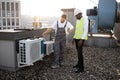 Repairmen standing and looking at conditioner on rooftop Royalty Free Stock Photo