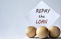 REPAY THE LOAN - words on a white piece of paper on a white background with wooden balls