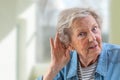 Repeat, please. Close-up of face of charming elderly woman is holding hand by her ear and struggling to hear something