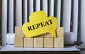 REPEAT - word on yellow paper against the background of wooden cubes and standing books