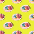 A repeating pattern of pink and blue donuts with a rainbow on a plate on a yellow background. Flat lay Royalty Free Stock Photo