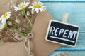 Repent, handwritten word with flowers and vintage paper envelope on wooden table