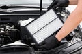 Replacing the air filter in a car. Auto mechanic in gray gloves holds an engine air filter against the engine Royalty Free Stock Photo