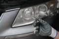Replacing light bulbs in car headlights. Auto mechanic in gloves holding high beam halogen bulb next to car headlight.