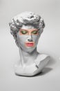 Replica of the head of an antique statue of David with a taped eyes and mouth with makeup on white background.