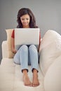 Replying to some emails. Full length shot of a young woman using her laptop while relaxing at home. Royalty Free Stock Photo