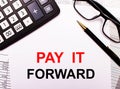 On the reports there is a calculator, glasses, a pen and a notebook with the inscription PAY IT FORWARD Royalty Free Stock Photo