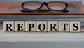 REPORTS - word on wooden cubes on the background of a folder with documents and glasses