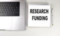 RESEARCH FUNDING text on notebook with laptop and pen