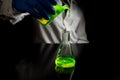 A research scientist experimenting with a green fluorescent droplets in a glass conical flask in dark biomedical laboratory for Royalty Free Stock Photo