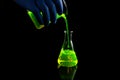 A research scientist experimenting with a green fluorescent droplets in a glass conical flask in dark biomedical laboratory for Royalty Free Stock Photo