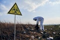 Researcher in protective suit collecting plastic garbage into black waste bag outdoors on a sunny day