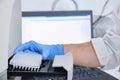 A researcher putting PCR plate on the thermal cycler for DNA amplification. Curve chart on monitor behind